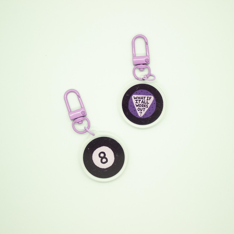 May include: Two purple and white keychains. One keychain features a purple eight ball with the number eight in white. The other keychain features a purple triangle with the text "What if it all works out?" in white.