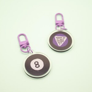 May include: Two purple and white keychains with a black and white 8 ball design and a purple triangle with the text "What if it all works out?"