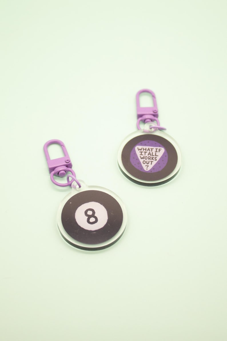 May include: Two purple and white keychains with a black and white 8 ball design and a purple triangle with the text "What if it all works out?"