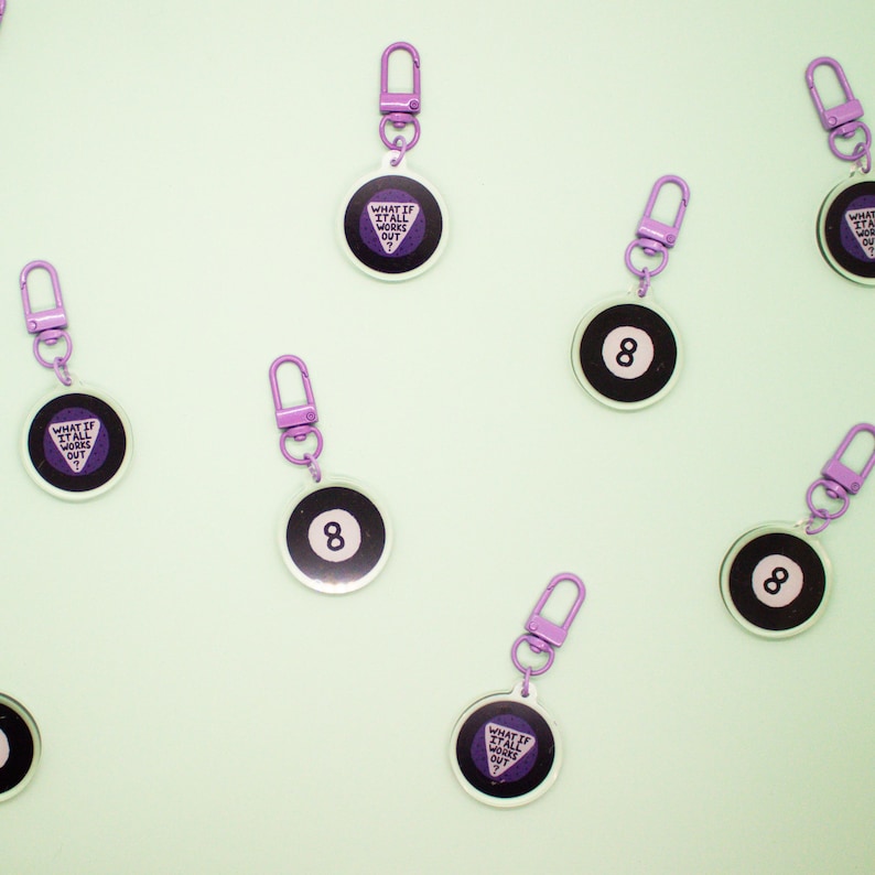 May include: Eight purple and black keychains with a purple eight ball design and a purple triangle with the text "What if it all works out?" on the other side.