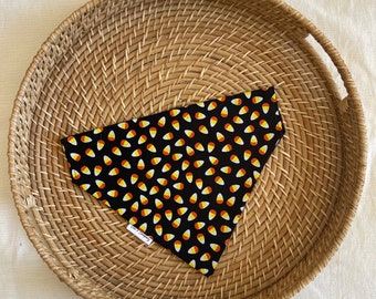 May include: Black bandana with a white and orange candy corn pattern. The bandana is on a woven tray.