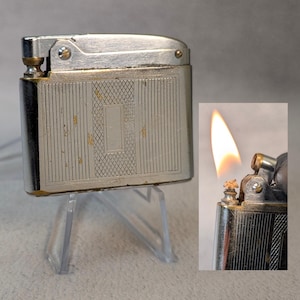 Puede incluir: Un encendedor plateado con un diseño texturizado y una pequeña llama que sale de la parte superior.