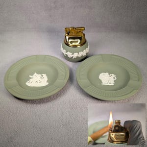 Pode incluir: Um cinzeiro de cerâmica verde com um desenho branco de uma mulher montando um unicórnio. Há um isqueiro de cerâmica verde combinando com uma parte superior dourada.