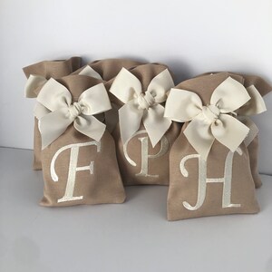 May include: Four small burlap gift bags with white satin bows and personalized with the letters F, P, and H in white embroidery.