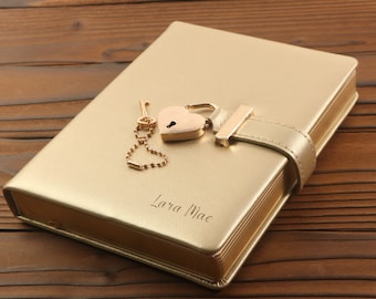 May include: A gold-colored journal with a heart-shaped lock and key. The journal has a leather cover and is engraved with the name "Lara Mae".