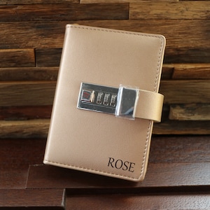 Può includere: Un diario in pelle color oro con un lucchetto a combinazione e la parola "ROSE" impressa sul davanti.