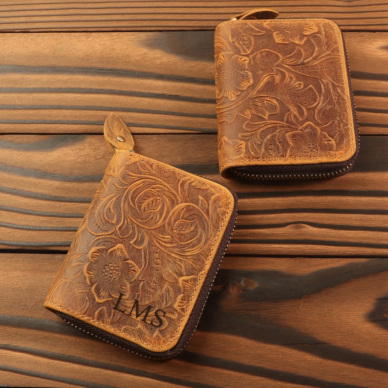 May include: Two brown leather zippered wallets with floral embossed designs. The wallet on the left has the initials "LMS" embossed on the front.