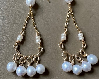 Peut inclure: Une paire de boucles d'oreilles pendantes en or avec des perles blanches. Les boucles d'oreilles ont une forme de larme et sont faites avec un design de chaîne à maillons. Les perles sont de tailles différentes et sont enfilées sur la chaîne.