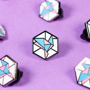 May include: A collection of hexagonal pins with a geometric design in shades of pink, blue, and white. The pins are arranged on a purple background.