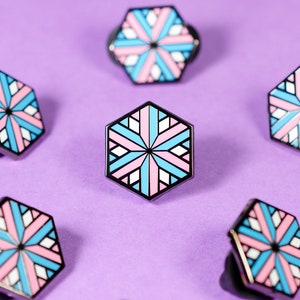 May include: A collection of 15 hexagonal pins featuring a geometric design in shades of pink, blue, and white. The pins are arranged in a grid pattern on a purple background.