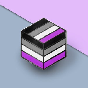 Op de afbeelding: Een zwarte, grijze en paarse emaille pin in de vorm van een kubus. De pin heeft de kleuren van de asexuele pride-vlag.