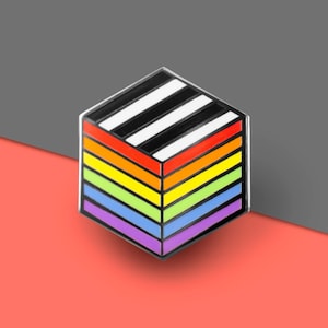 May include: A rainbow-colored enamel pin in the shape of a cube with black and white stripes on the top. The pin is made of metal and has a silver finish.