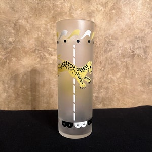May include: Frosted glass tumbler featuring a yellow and black cheetah design. The tumbler has a white and gold decorative top and a black base with a repeating pattern. The design is reminiscent of a carousel.