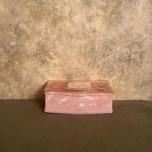 May include: A rectangular storage box with a pink and white marbled base and a translucent, light pink lid. The lid features a subtle grid pattern on its top surface. The box has a clean, structured design with smooth, rounded corners.