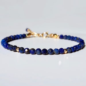 May include: A delicate bracelet featuring faceted, deep blue lapis lazuli beads. The bracelet is strung on a gold-colored chain and includes a gold-colored clasp and small gold beads. The bracelet is designed for everyday wear.
