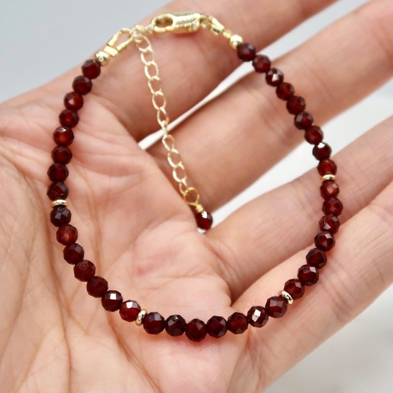 Pu&ograve; includere: Un braccialetto delicato con piccole perline sfaccettate di colore rosso scuro. Il braccialetto presenta dettagli color oro e una chiusura abbinata con una catena di estensione. Le perline sono distanziate in modo uniforme, creando un design simmetrico ed elegante.