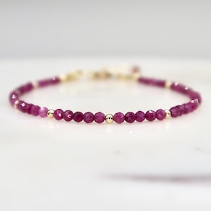 May include: A delicate bracelet made with small, faceted ruby beads and gold accents.