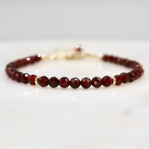 Pu&ograve; includere: Un delicato braccialetto con perline di granato rosso intenso sfaccettate. Le perline sono infilate con una catena e dettagli dorati, creando un gioiello semplice ma elegante. Il braccialetto &egrave; progettato per essere indossato come accessorio.