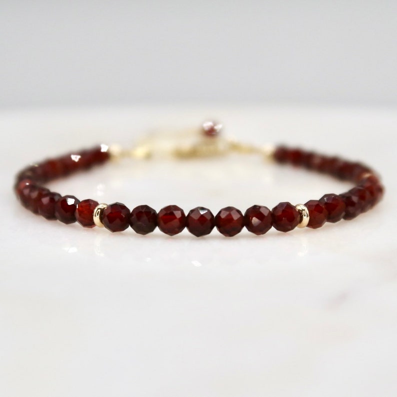 Pu&ograve; includere: Un delicato braccialetto con perline di granato rosso intenso sfaccettate. Le perline sono infilate con una catena e dettagli dorati, creando un gioiello semplice ma elegante. Il braccialetto &egrave; progettato per essere indossato come accessorio.