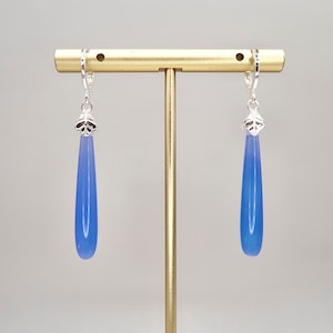 May include: A pair of silver teardrop earrings with blue gemstone drops hanging from a gold stand.