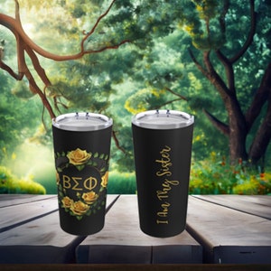 May include: Two black stainless steel tumblers with gold lettering. One tumbler features a gold floral design with the letters "BΣΦ" in the center. The other tumbler has the text "I Am They Sister".
