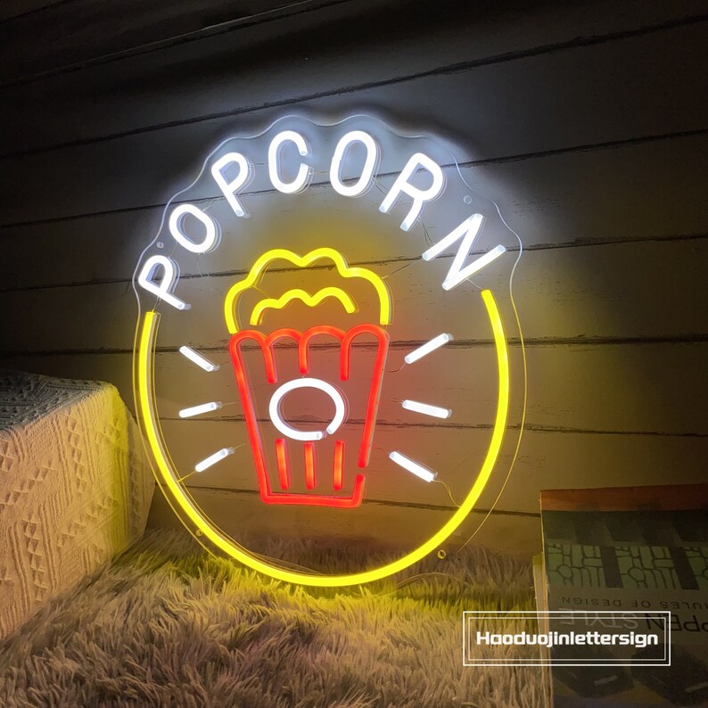 May include: A yellow neon sign with the word "POPCORN" in white neon letters and a red and yellow neon image of a popcorn bucket with popcorn on top.