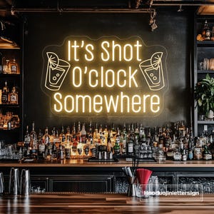 Puede incluir: Un letrero de neón amarillo con el texto "It's Shot O'clock Somewhere" e ilustraciones de cócteles. El letrero está montado en una pared oscura detrás de una barra, con botellas y vasos.