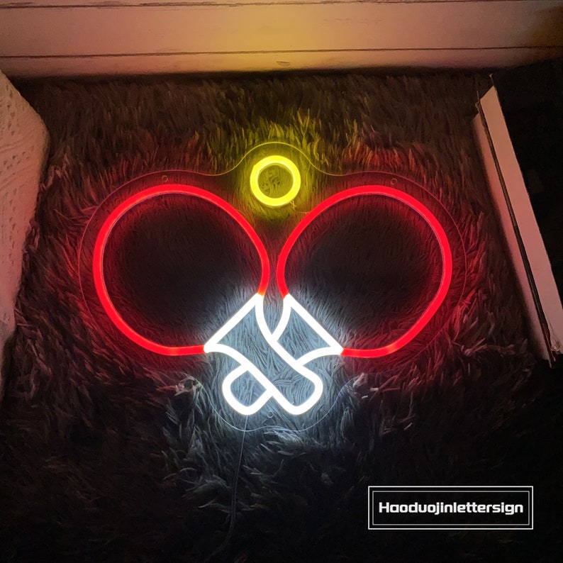 May include: Neon sign depicting two red ping pong paddles with a white neon ball in the middle. The sign is on a fuzzy brown surface. The text "Haoduujinletterssign" is visible in the bottom right corner of the image.