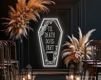 May include: A neon sign in the shape of a coffin with the words "Til Death Do Us Part" and the date 12-16-2025. The sign is surrounded by floral arrangements and candles, creating a gothic wedding theme.