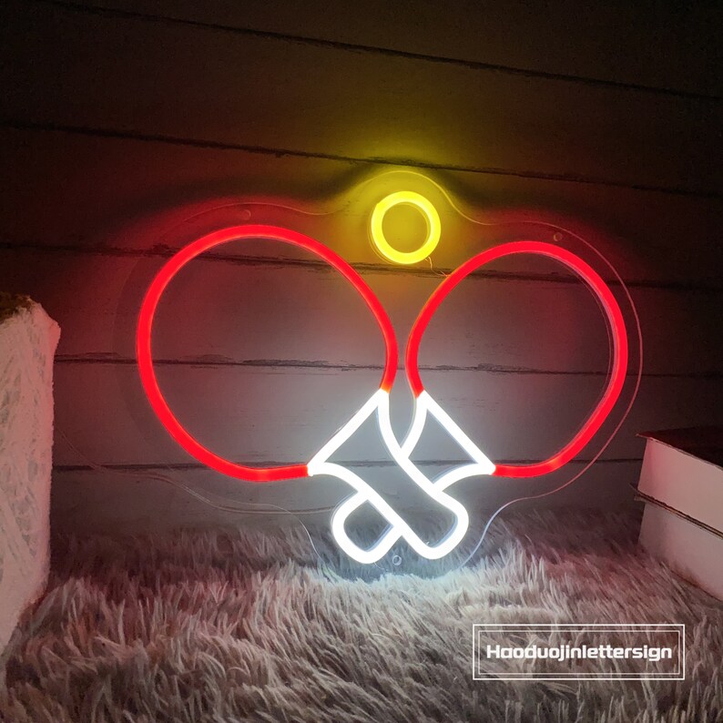 May include: Neon sign depicting two red ping pong paddles with a white ball in the middle. The sign is on a clear background.