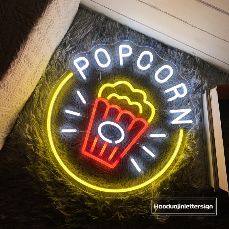May include: Yellow neon sign with the word "POPCORN" in white letters and a red and yellow popcorn bucket graphic.