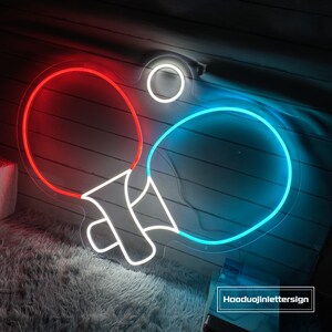 May include: A neon sign shaped like two ping pong paddles, one red and one blue, with a white neon ball in the center. The sign is mounted on a clear acrylic backing. The text "Haoduujinlettersign" is visible in the bottom right corner of the image.