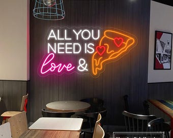 May include: A neon sign with the words "ALL YOU NEED IS Love &" and a pizza slice with heart-shaped pepperoni. The sign is mounted on a dark wood-paneled wall in a restaurant setting. Tables and chairs are visible.