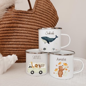 Könnte beinhalten: Drei weiße Emaille-Tassen mit silbernen Rändern. Eine Tasse zeigt einen blauen Wal und den Namen Jakob. Eine weitere zeigt einen hellgrünen Van mit Safari-Tieren und den Namen Samuel. Die dritte Tasse zeigt einen braunen Bären und den Namen Amelie.