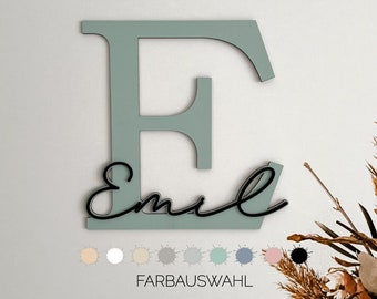 Puede incluir: Una gran letra E de madera verde claro con el nombre "Emil" escrito en cursiva negra debajo. Debajo de la letra se muestra una paleta de colores beige, blanco, gris, verde claro, azul, rosa y negro.