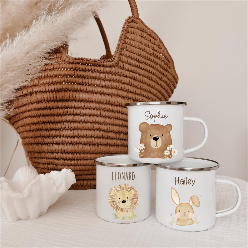 May include: Three white enamel mugs with silver rims, each featuring a unique animal illustration and a name. One mug shows a bear with the name Sophie, another a lion with the name Leonard, and the third a rabbit with the name Hailey printed above.