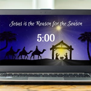 May include: A laptop screen shows a Christmas graphic with a night sky, star, and silhouettes of palm trees, camels, and a nativity scene. Text reads "Jesus is the Reason for the Season" and "5:00".