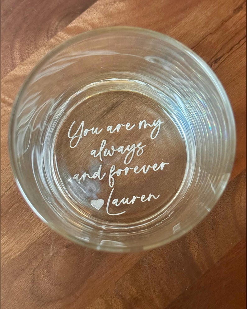 May include: A clear glass tumbler with etched text that reads "You are my always and forever Lauren" with a heart symbol. The glass is round and sits on a wooden surface.