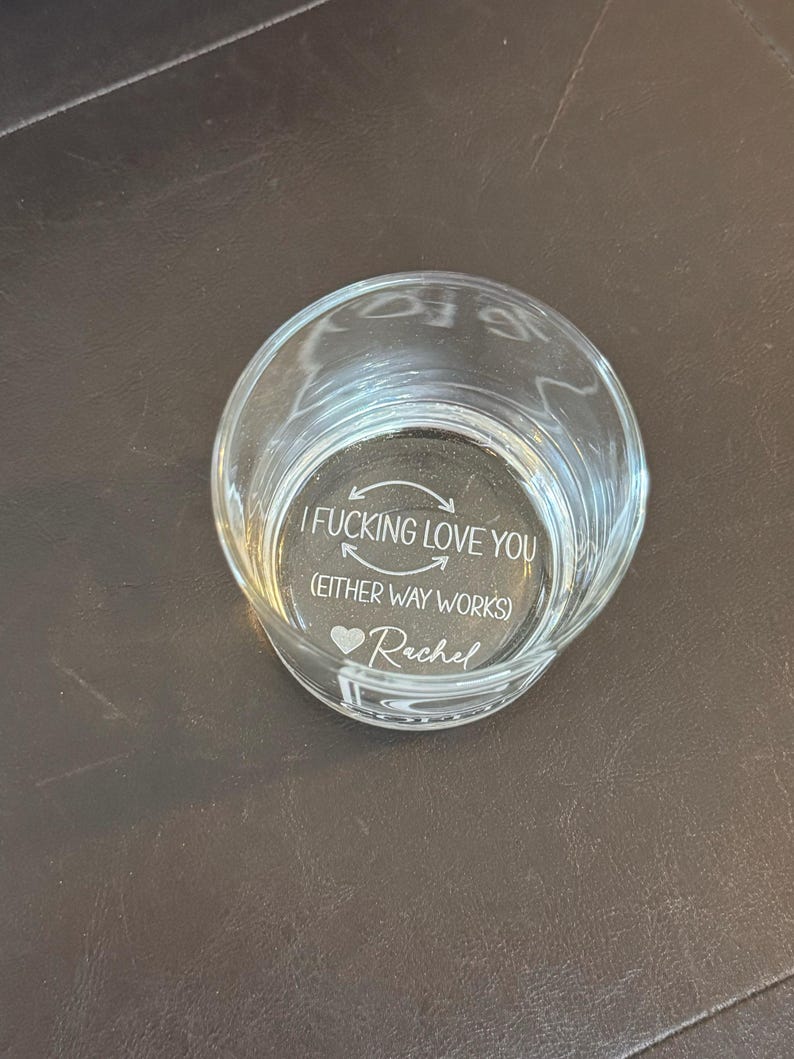 May include: A clear glass votive candle holder with etched text. The text reads "I FUCKING LOVE YOU (EITHER WAY WORKS) ❤️ Rachel". The candle holder is round and sits on a dark surface.