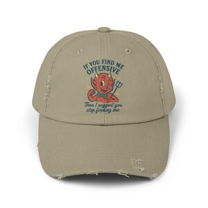 Puede incluir: Gorra de béisbol caqui desgastada con un diablo de dibujos animados y la frase "IF YOU FIND ME OFFENSIVE Then I suggest you stop finding me" en estilo vintage.