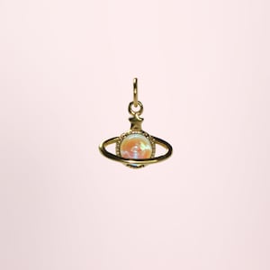 Peut inclure: Pendentif doré en forme de planète, avec un anneau autour d'un globe central. Le globe présente un aspect nacré et irisé, avec des teintes orangées et roses. Le pendentif est suspendu à une petite boucle.