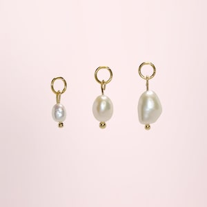 Peut inclure: Trois breloques en perles dorées de différentes formes et tailles. Chaque breloque est ornée d'une petite perle dorée ronde en bas et d'un anneau doré en haut pour l'attache. Les perles sont blanches et ont un éclat brillant.