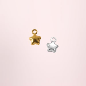 May include: Two small star-shaped charms, one in a matte gold finish and one in a polished silver finish. Each charm features a rounded, puffed design and includes a small circular jump ring at the top for attachment to jewellery or accessories.