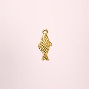 Può includere: Un piccolo ciondolo a forma di pesce dorato con un motivo a scaglie strutturate. Il ciondolo ha un anello nella parte superiore per il fissaggio a una collana o un braccialetto. Il pesce è un design semplice ed elegante, adatto alla creazione di gioielli.