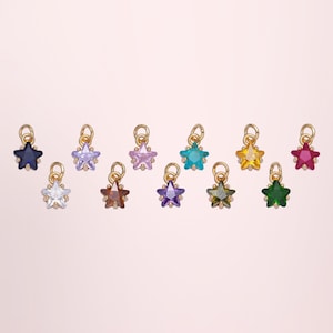 May include: A collection of eleven small star-shaped charms, each featuring a faceted gemstone in a different colour including blue, purple, pink, teal, yellow, red, clear, brown, violet, olive green, and emerald green, all set in gold-toned metal.