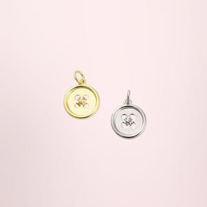 May include: Two circular button charms, one in a polished gold tone and one in a polished silver tone. Each charm features a classic four-hole design in the centre and includes a small jump ring at the top for attachment to a chain or bracelet.