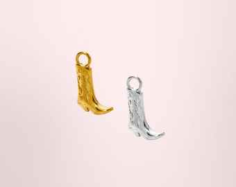 Puede incluir: Dos dijes de metal con forma de botas vaqueras, uno en tono dorado pulido y otro en tono plateado pulido. Cada dije de bota presenta patrones de costura decorativos en relieve en la caña y una pequeña anilla circular en la parte superior.