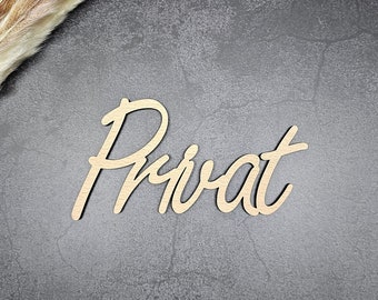 May include: A wooden sign with the word "Privat" written in cursive script. The sign is on a dark gray background with dried pampas grass in the top left corner.