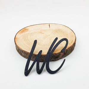 May include: Black wooden cutout of the letters "WC" on a natural wood slice.