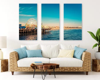 May include: A triptych wall art set featuring a coastal pier with a large Ferris wheel, ocean waves, and a clear blue sky. The three vertical panels display a continuous panoramic view of a beach scene during the day with warm sunlight.